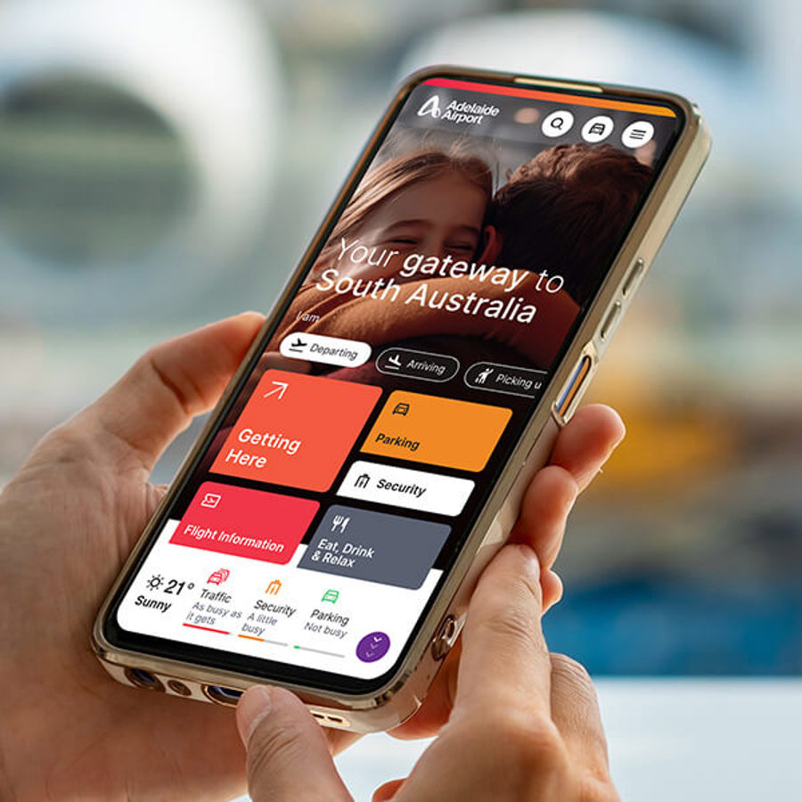 A person inside Adelaide airport holding their mobile phone with the Adelaide airport homepage on the screen
