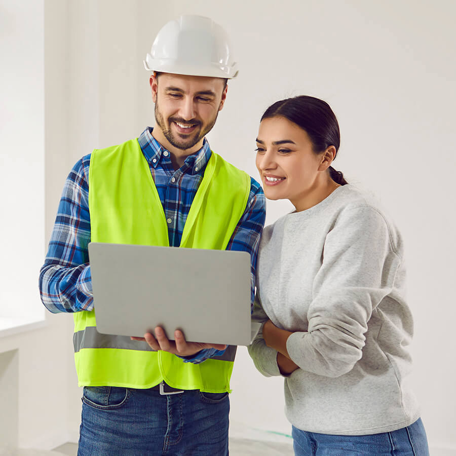 A building surveyor showing a female homeowner a webpage on his laptop screen.