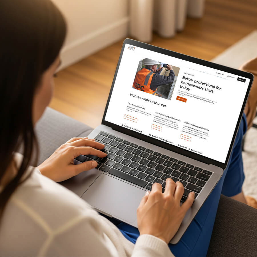 A woman sitting in her living room, looking at the BPC homeowners webpage on her laptop, which is on her lap.