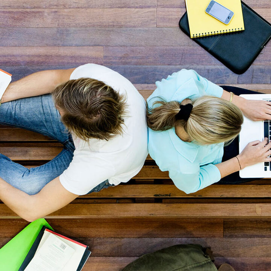 Image of two people sitting back to back working on laptops