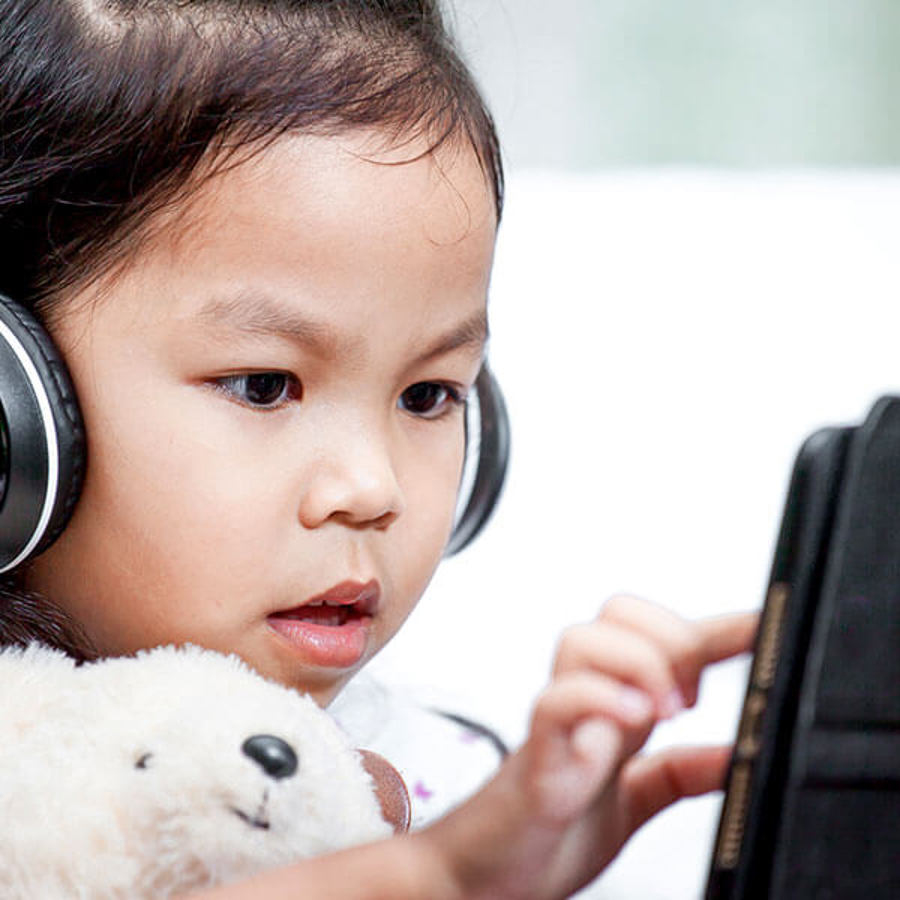 Child with headphones on device with teddy bear